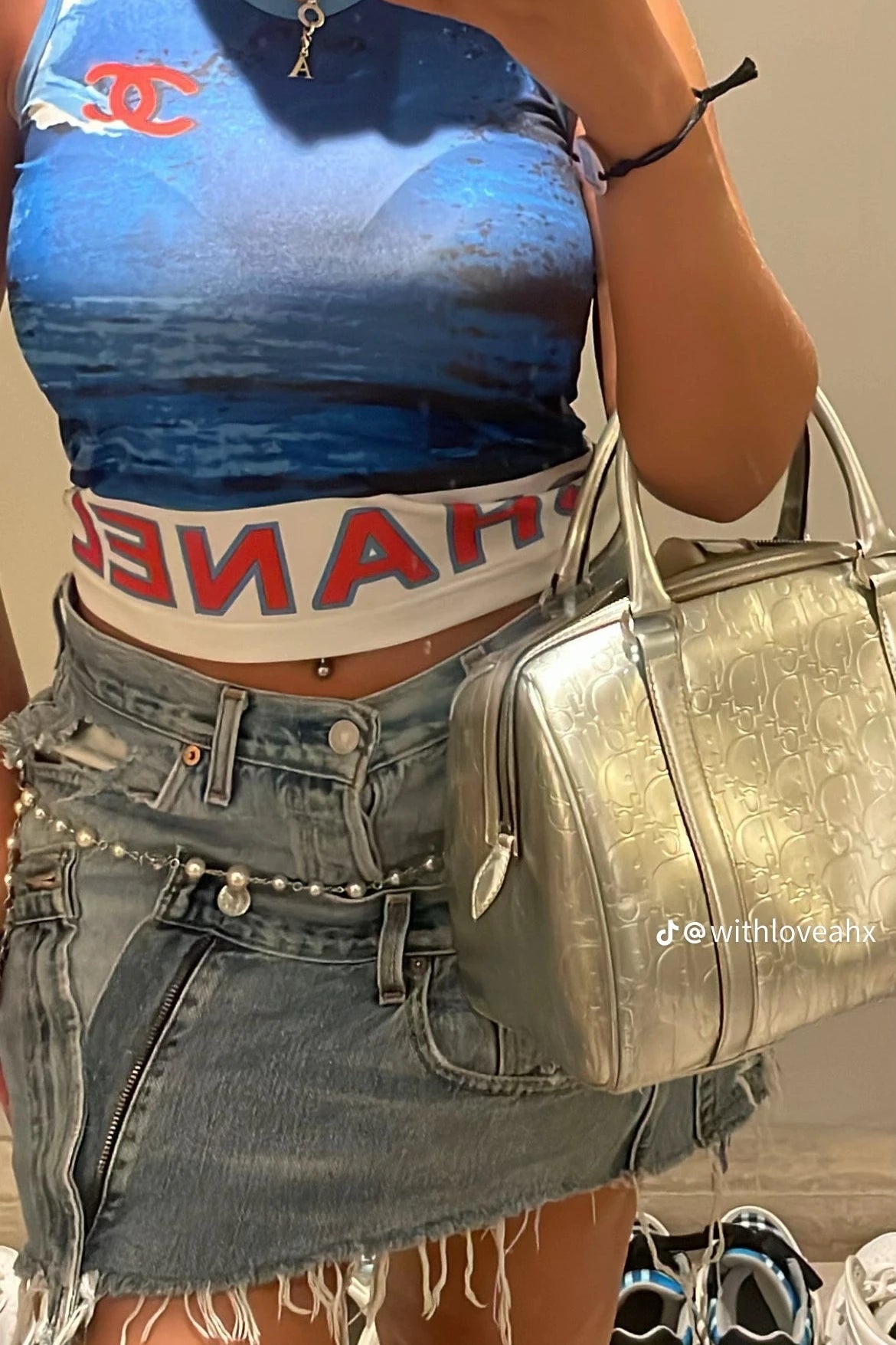 Person wearing a blue and white tank top with red text, holding a silver handbag.