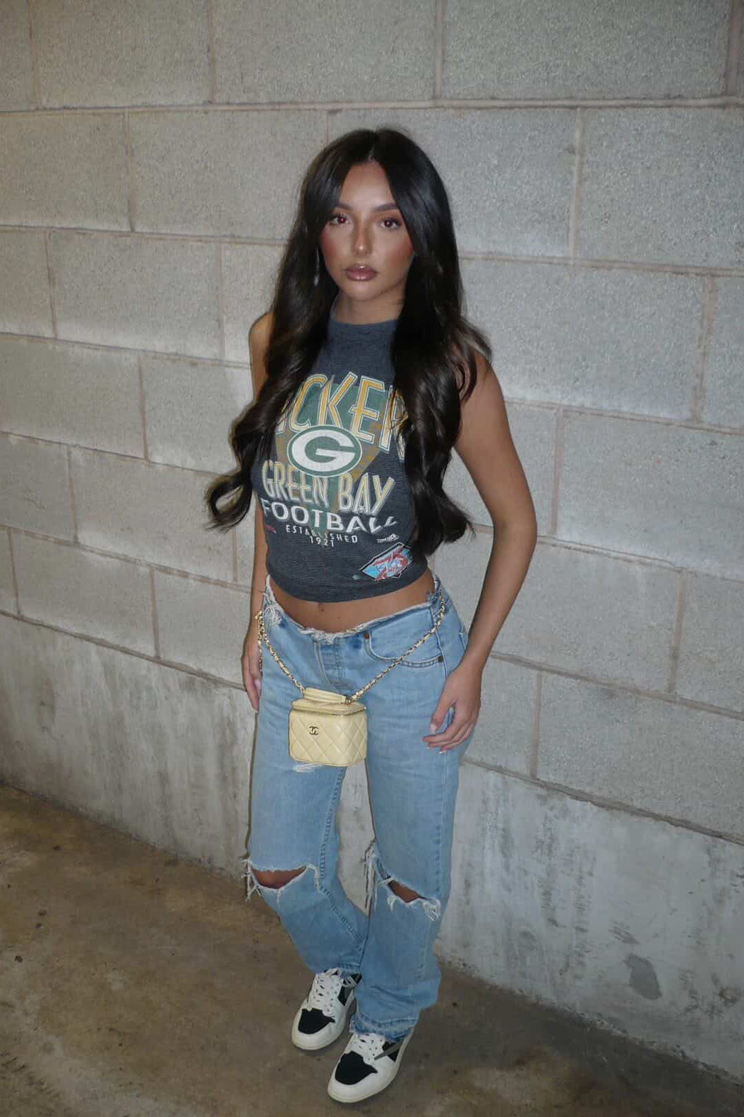 Person wearing a graphic t-shirt and ripped jeans standing against a concrete wall.