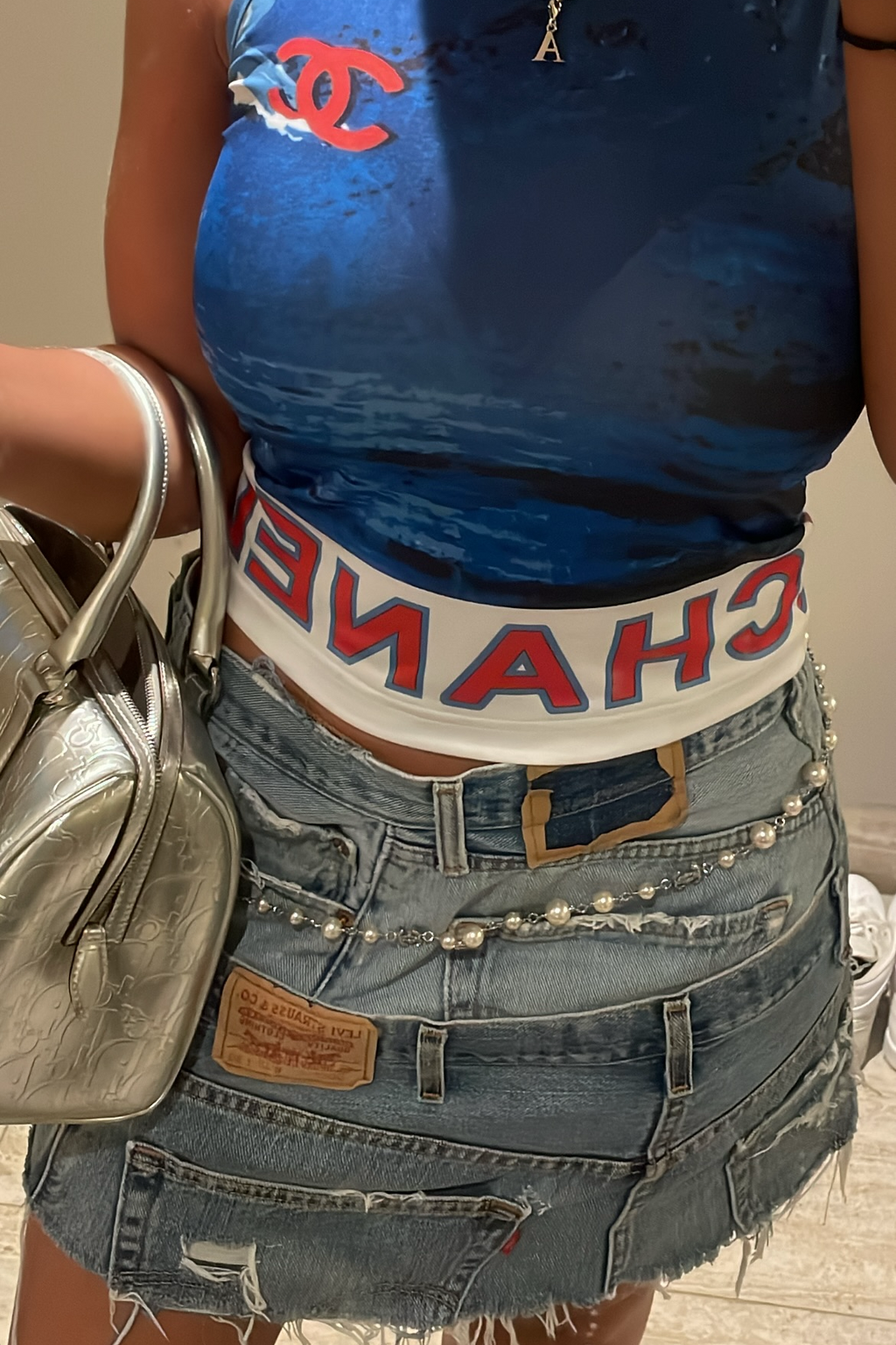 Person wearing a blue tank top with a red logo, denim shorts, and carrying a silver handbag.