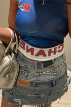 Person wearing a blue tank top with a red logo, denim shorts, and carrying a silver handbag.