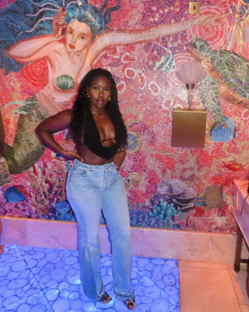 Person posing in front of a colorful mural in a room with a blue floor.