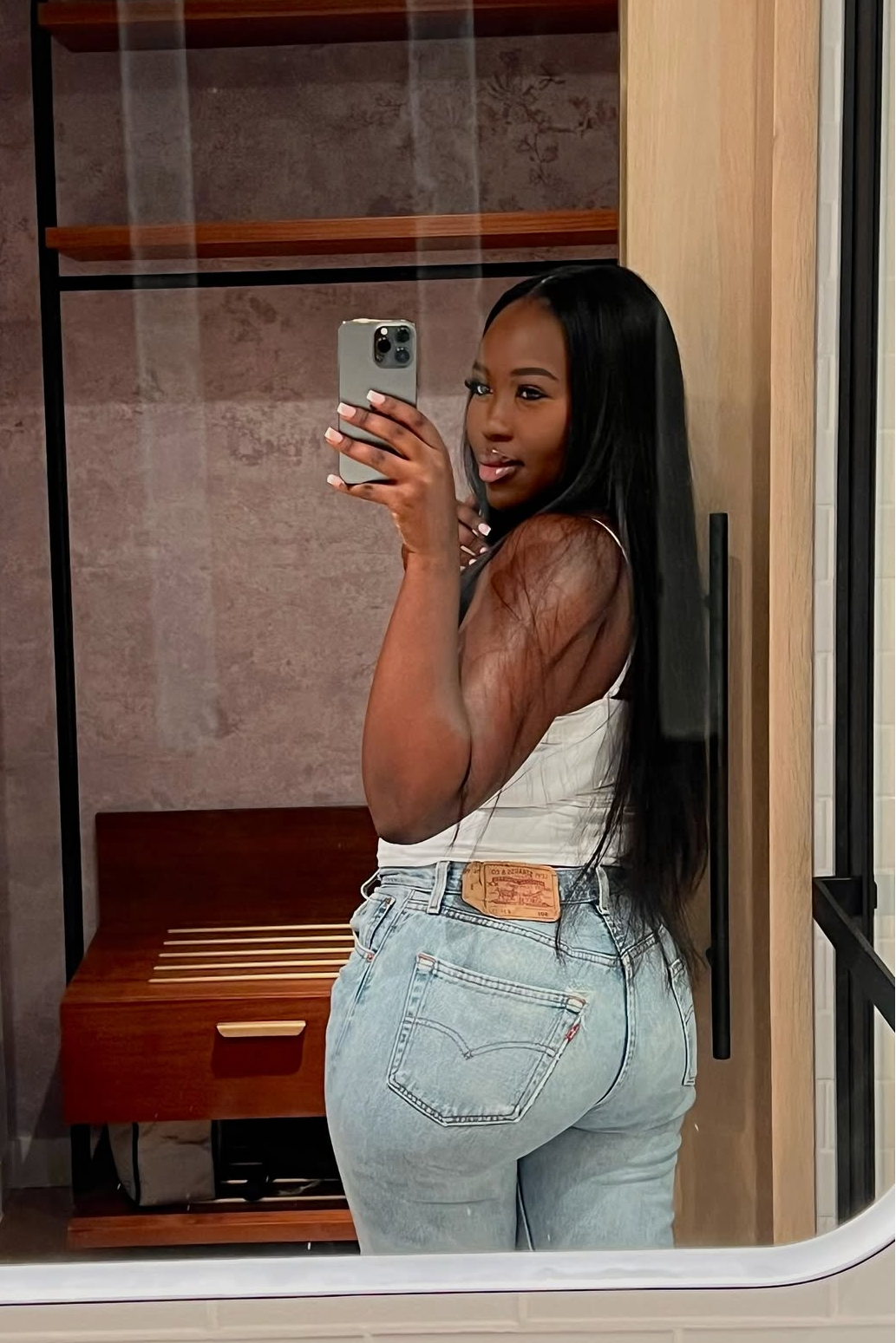 Person taking a mirror selfie wearing a white top and light blue jeans in a room.