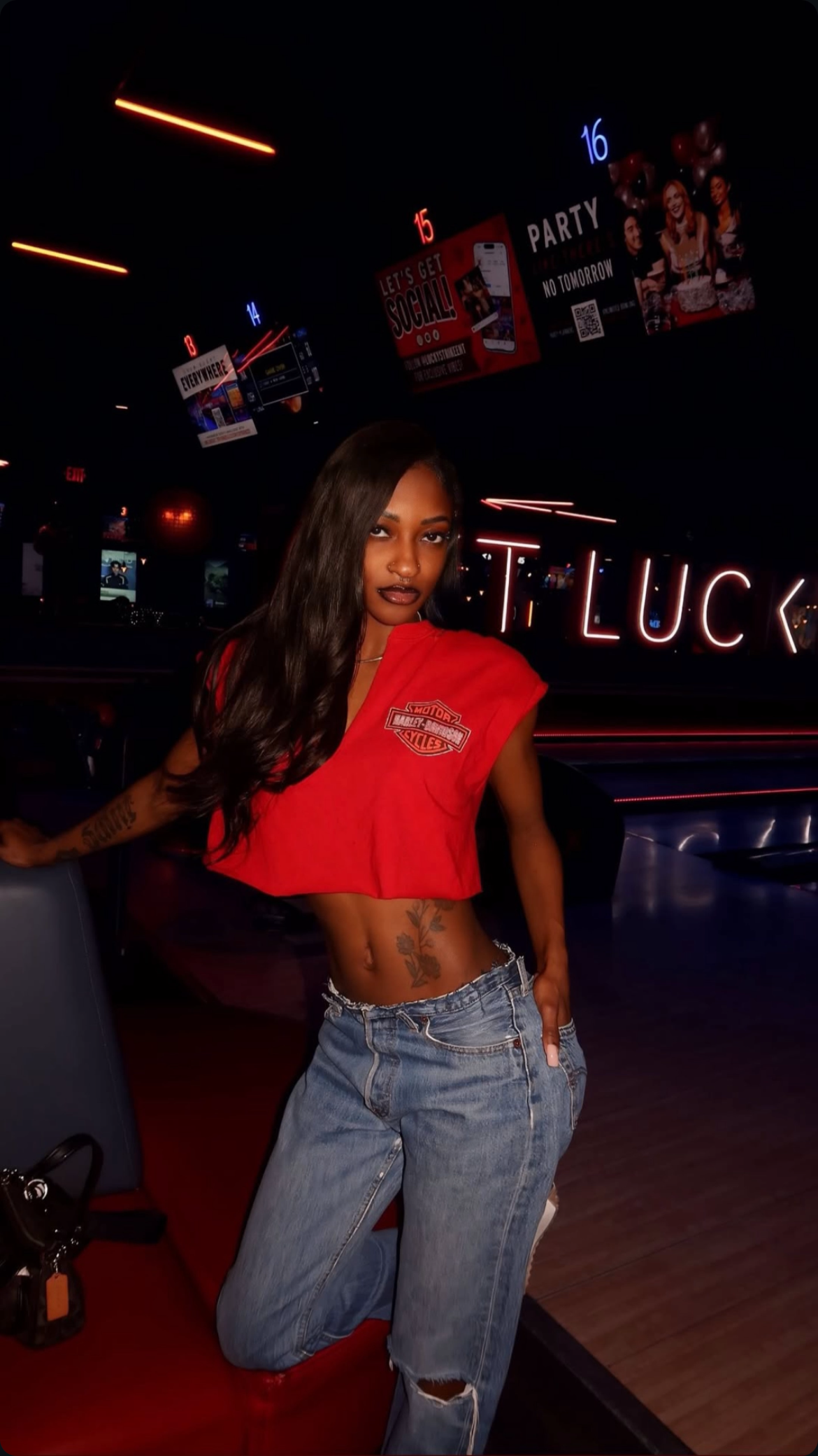 Person wearing a red crop top and blue jeans in a bar setting with neon signs.