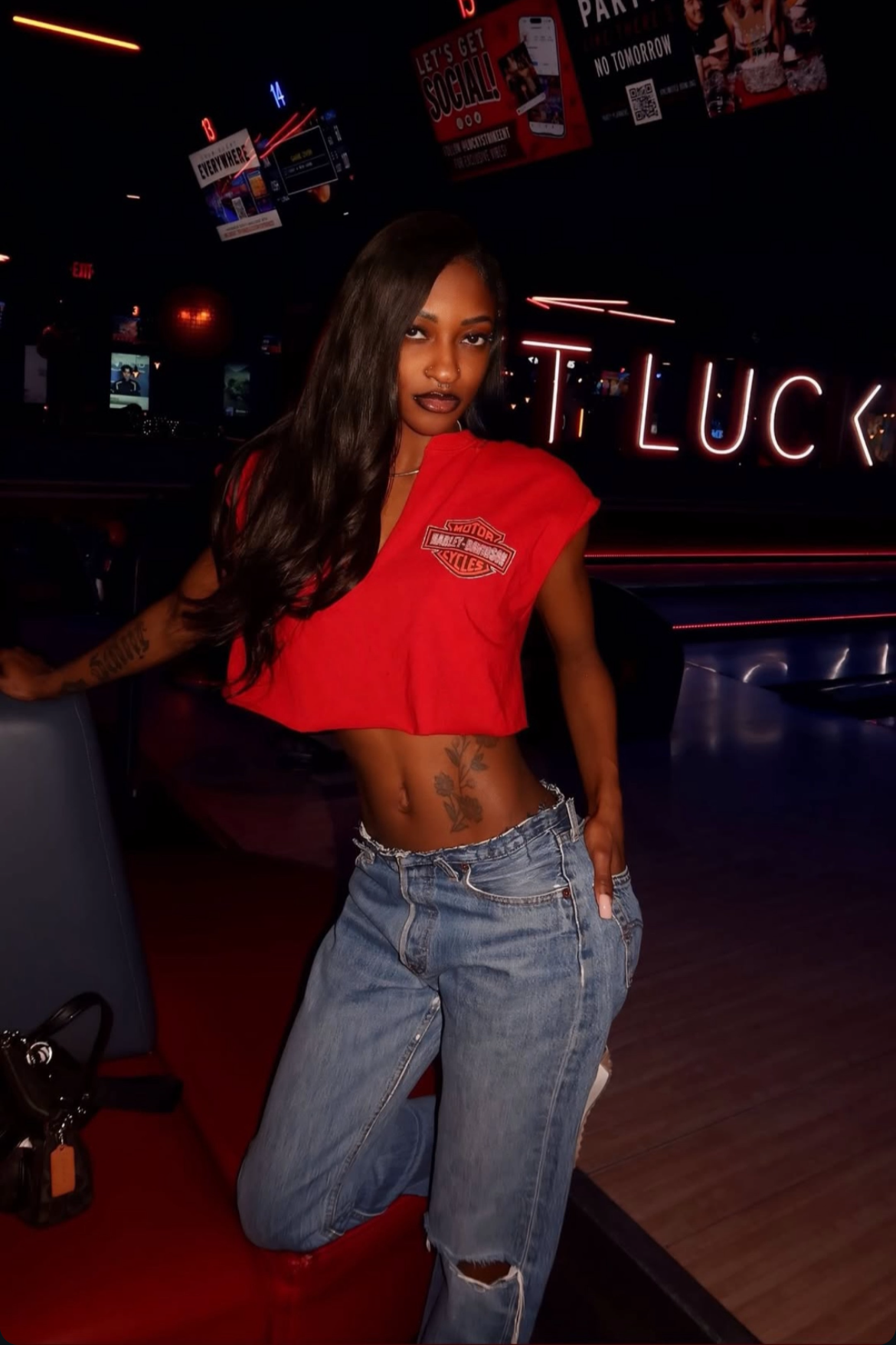 Person wearing a red crop top and blue jeans in a bar setting with neon signs.