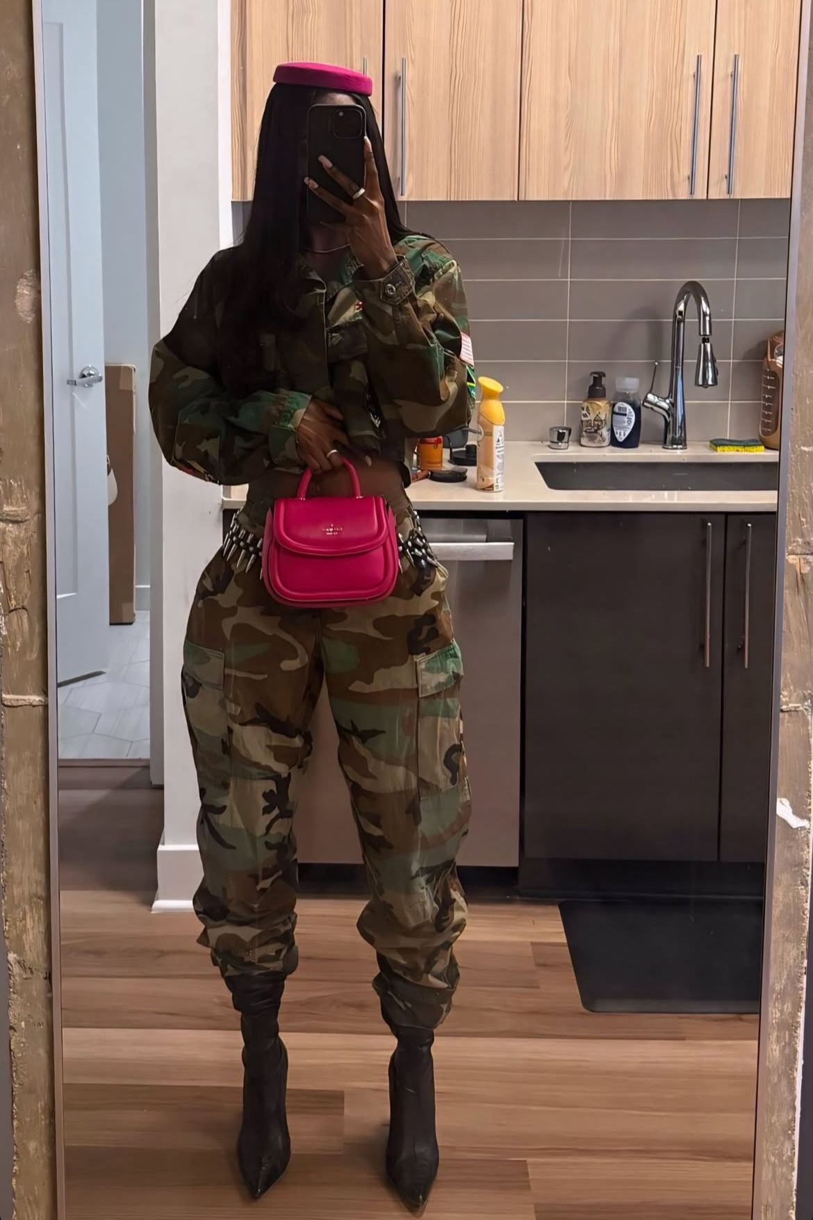 Person wearing a camouflage outfit with a pink bag in a kitchen.