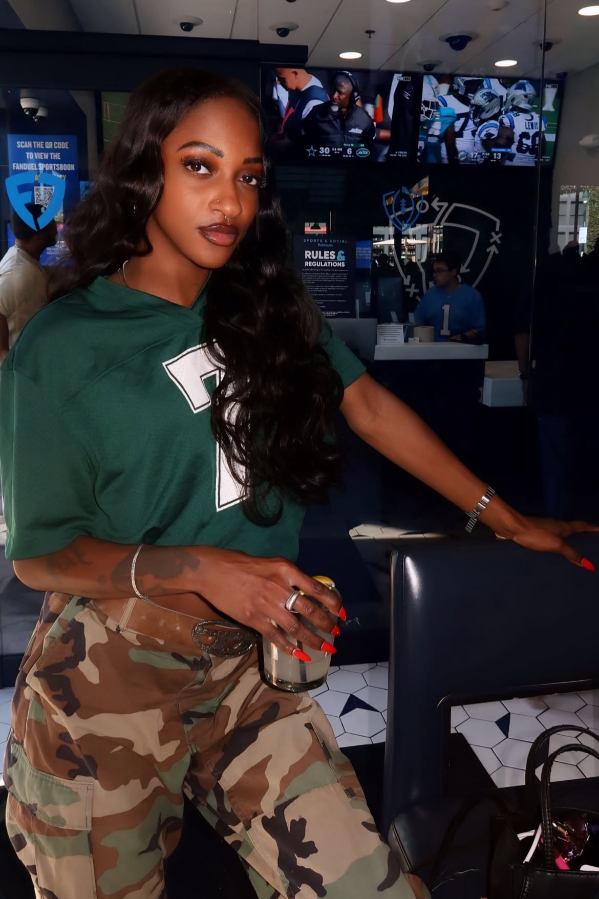 Woman in a green shirt and custom vintage camouflage pants standing in a sports bar with multiple televisions on the wall | closet luna