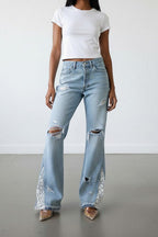 Woman wearing a white t-shirt and light blue ripped jeans against a plain background